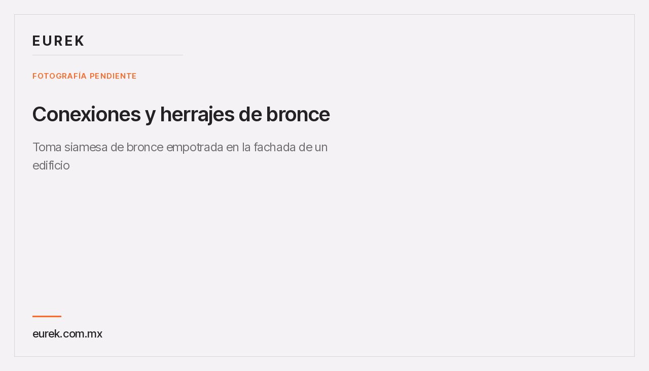 Toma siamesa de bronce empotrada en la fachada de un edificio