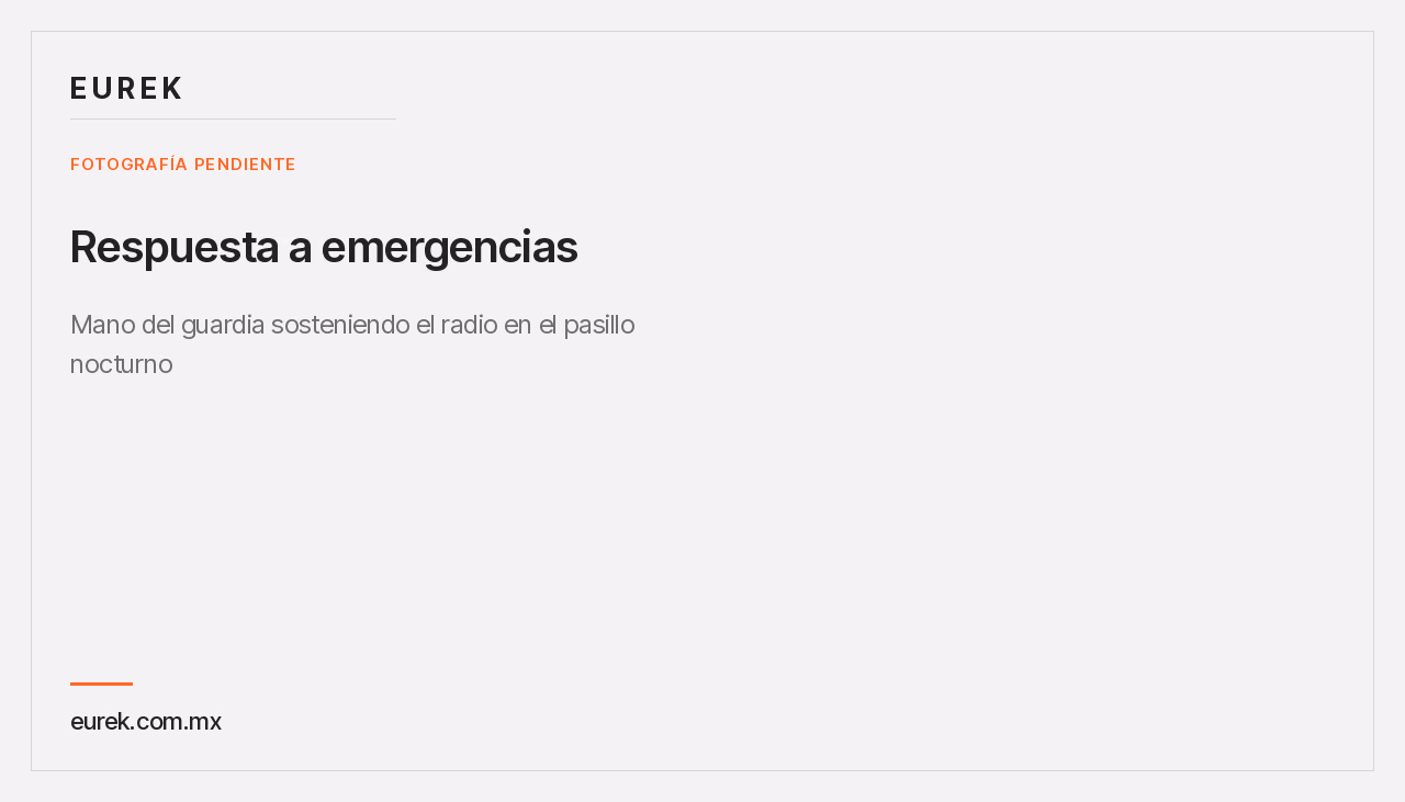 Mano del guardia sosteniendo el radio en el pasillo del condominio de noche, con la iluminación de emergencia detrás